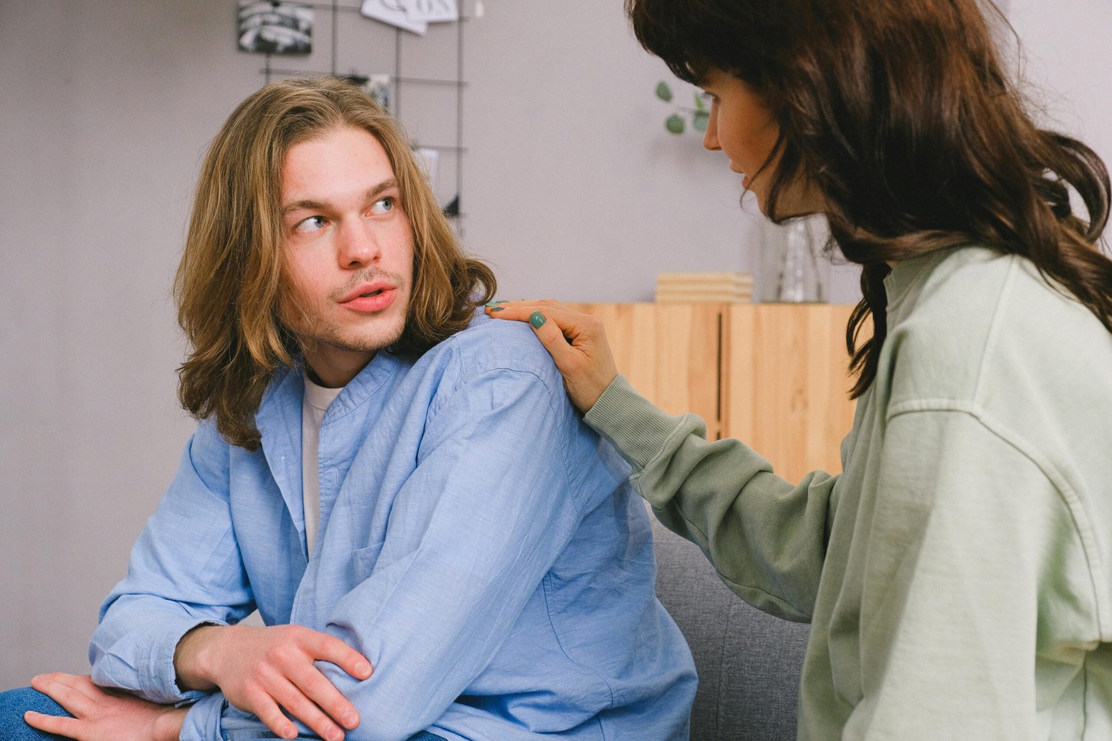 Concentrated woman talking and touching shoulder of pensive male in light room in daytime