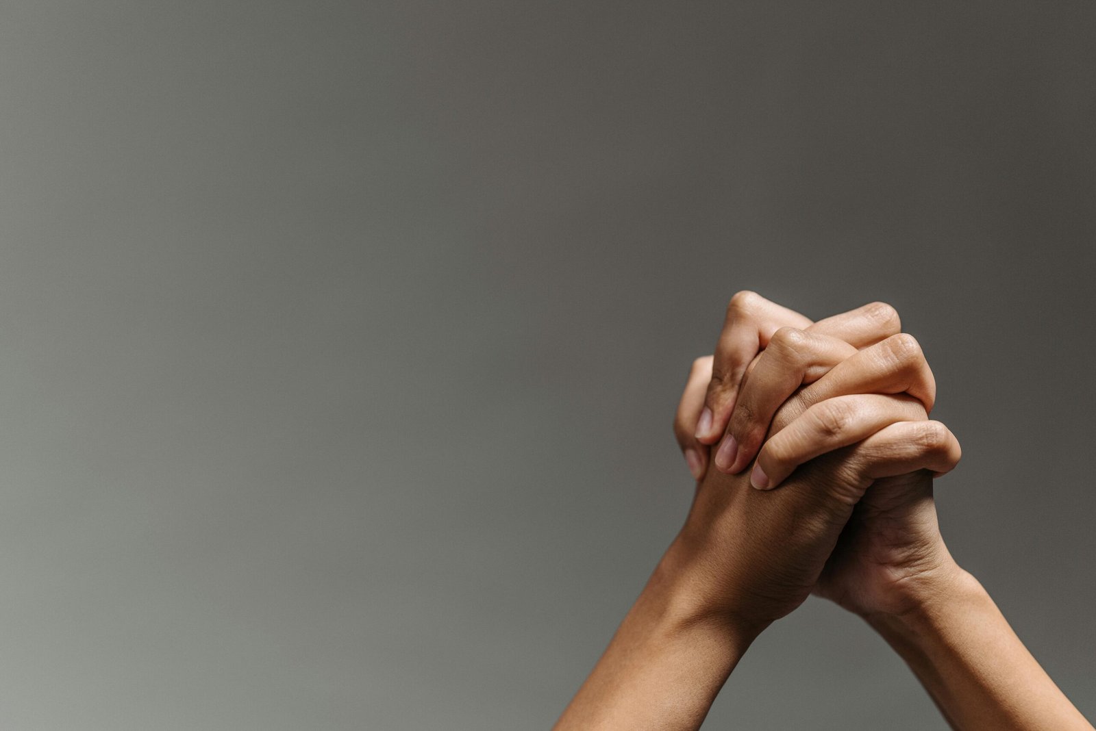 Close-up of two hands clasped together on a gray background, symbolizing unity and support.